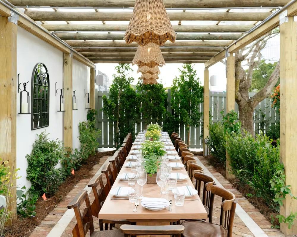 Wicker chandeliers above the long communal table beneath the pergola at Rosemary's Wynwood