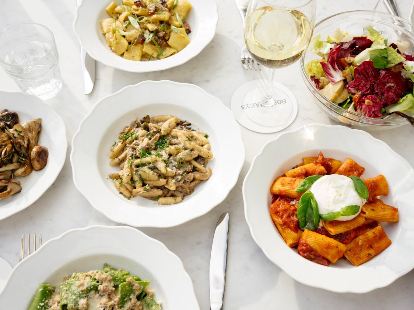 Housemade pastas, chopped salad and white wine on a marble table at Rosemary's Wynwood, Miami