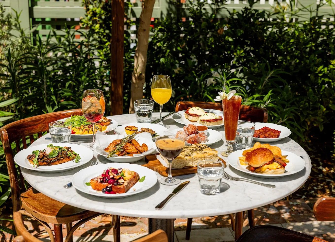A sunlit garden table with seasonal plates, cocktails and aperitivo at Rosemary's Wynwood, Miami