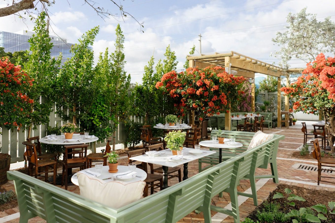 The garden terrace of Rosemary's Wynwood with sage green benches and orange bougainvillea in Miami's arts district