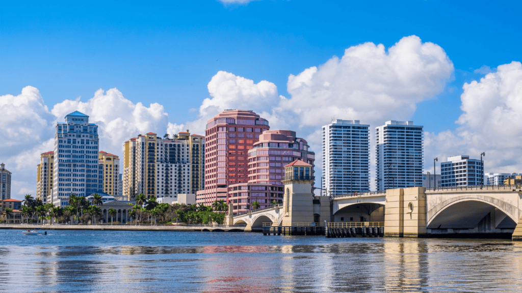 Coastal city skyline across blue water with an arched bridge and palm trees