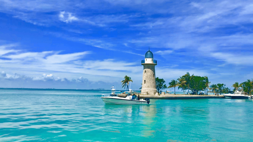 Stone lighthouse on a palm-lined jetty with a white motorboat in turquoise water