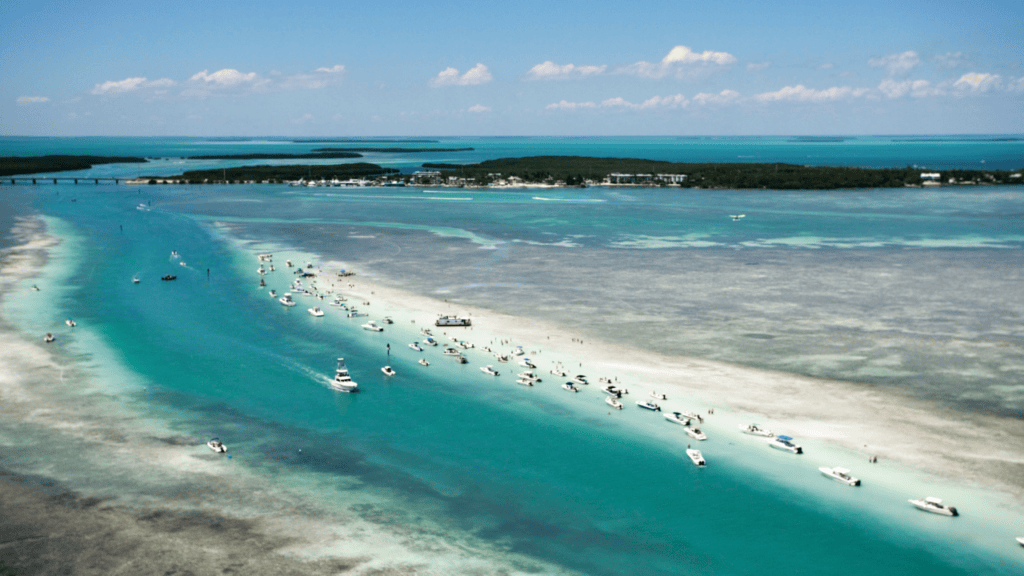 Aerial view of a white sandbar in turquoise water with boats anchored along the shallows