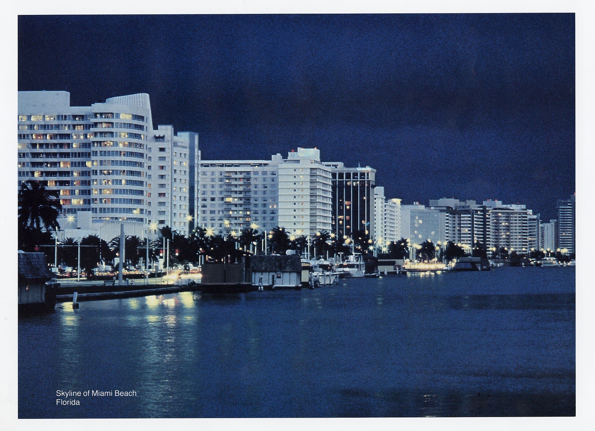 The Miami Beach skyline at twilight, with high-rise buildings and palm trees silhouetted against a deep blue sky over Biscayne Bay
