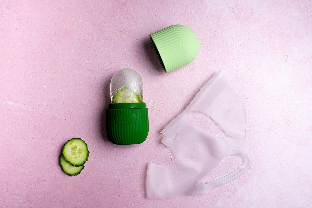 A skincare flat lay with cucumber slices, an ice roller with cucumber inside, and a silicone face mask — the cooling, hydrating ritual that defines Miami summer beauty