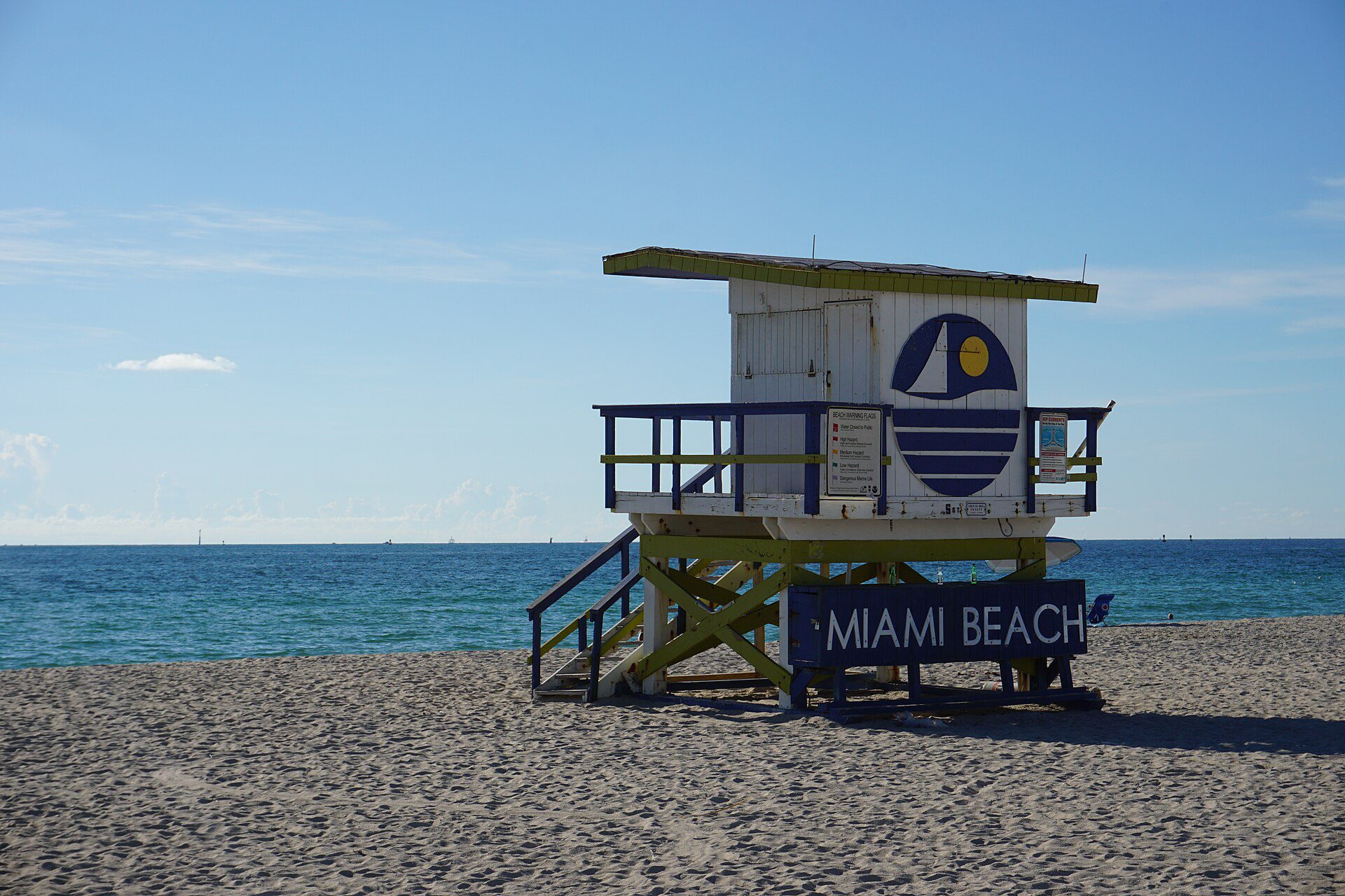 The iconic two-story Miami Beach lifeguard stand in white and blue with the MIAMI BEACH sign visible at the base, set against turquoise Atlantic waters
