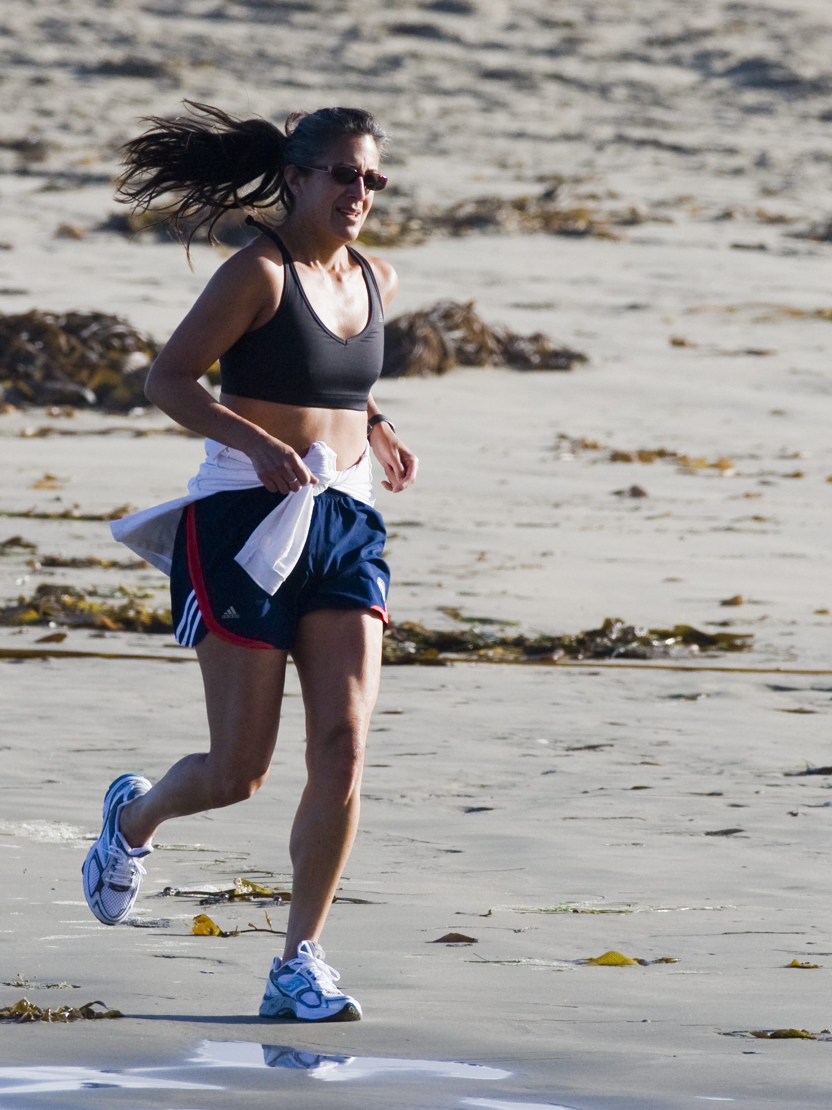 A fit runner in dark athletic wear captured mid-stride running along a sandy beach, embodying the recurring fitness ritual that defines Miami's run club culture
