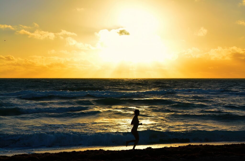 A runner silhouetted against the golden sunrise sky, running along the water's edge on Miami Beach with the Atlantic Ocean reflecting the morning light