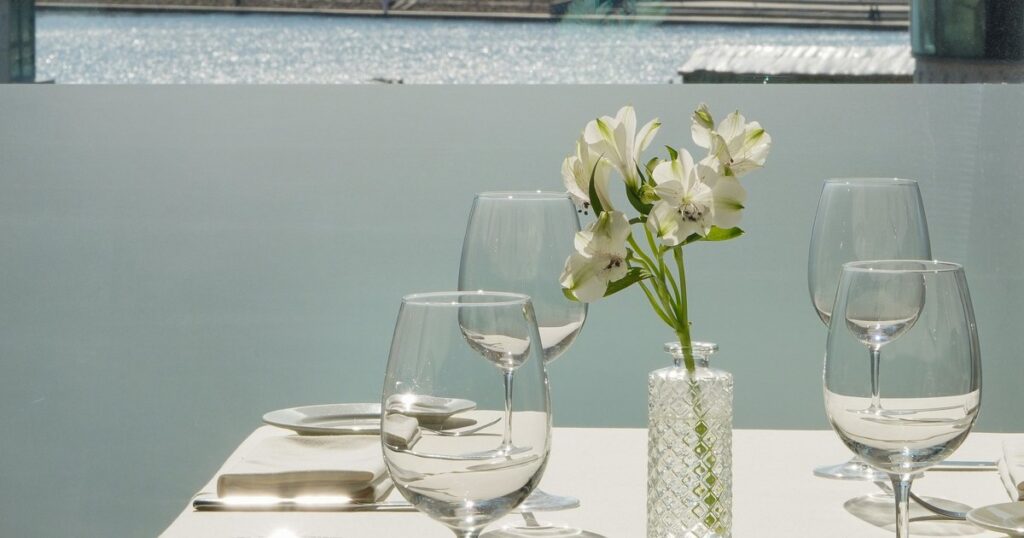 Wine glasses and flowers on a white table with the bay behind