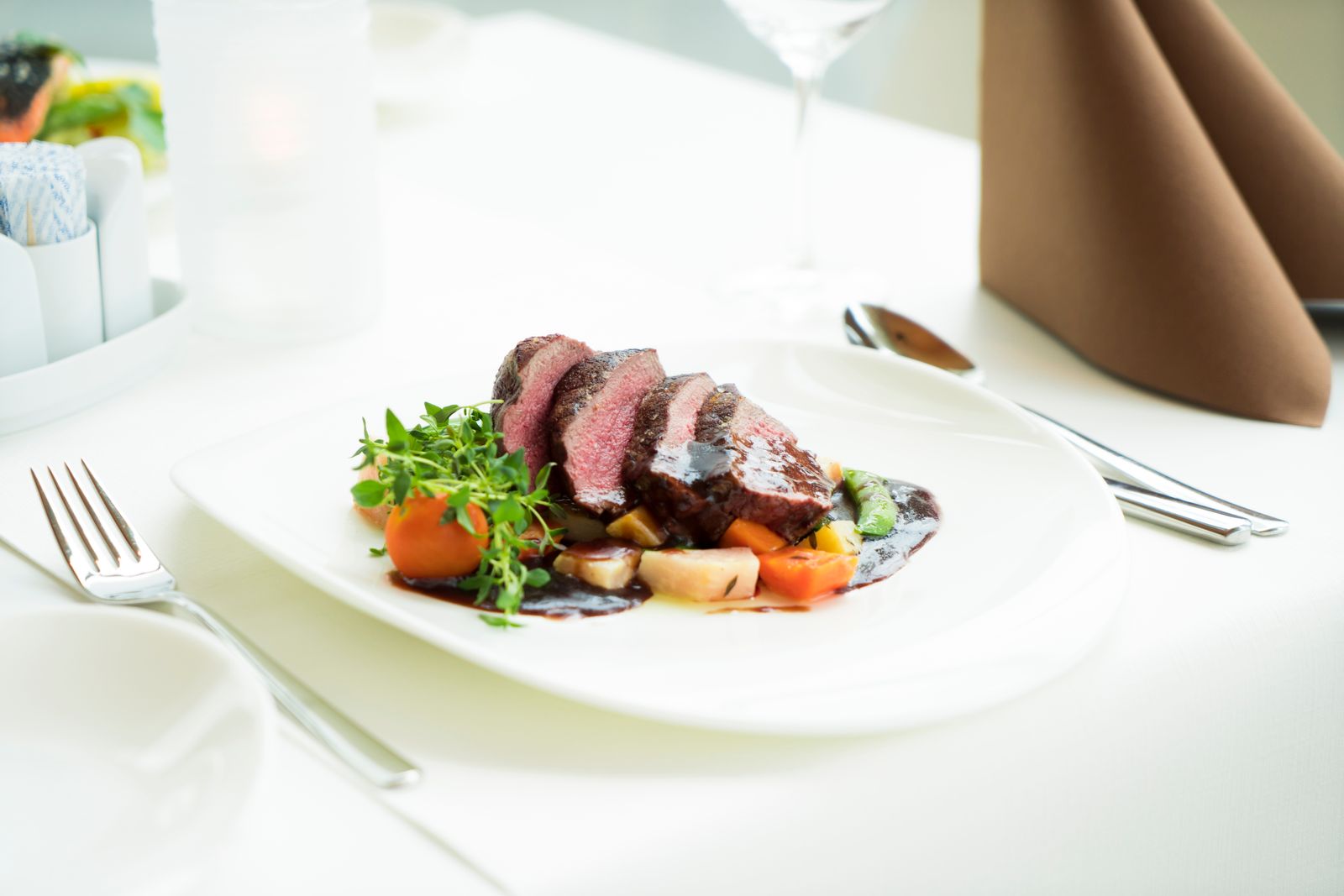 Sliced steak with vegetables and red wine sauce on a white plate in a fine dining setting