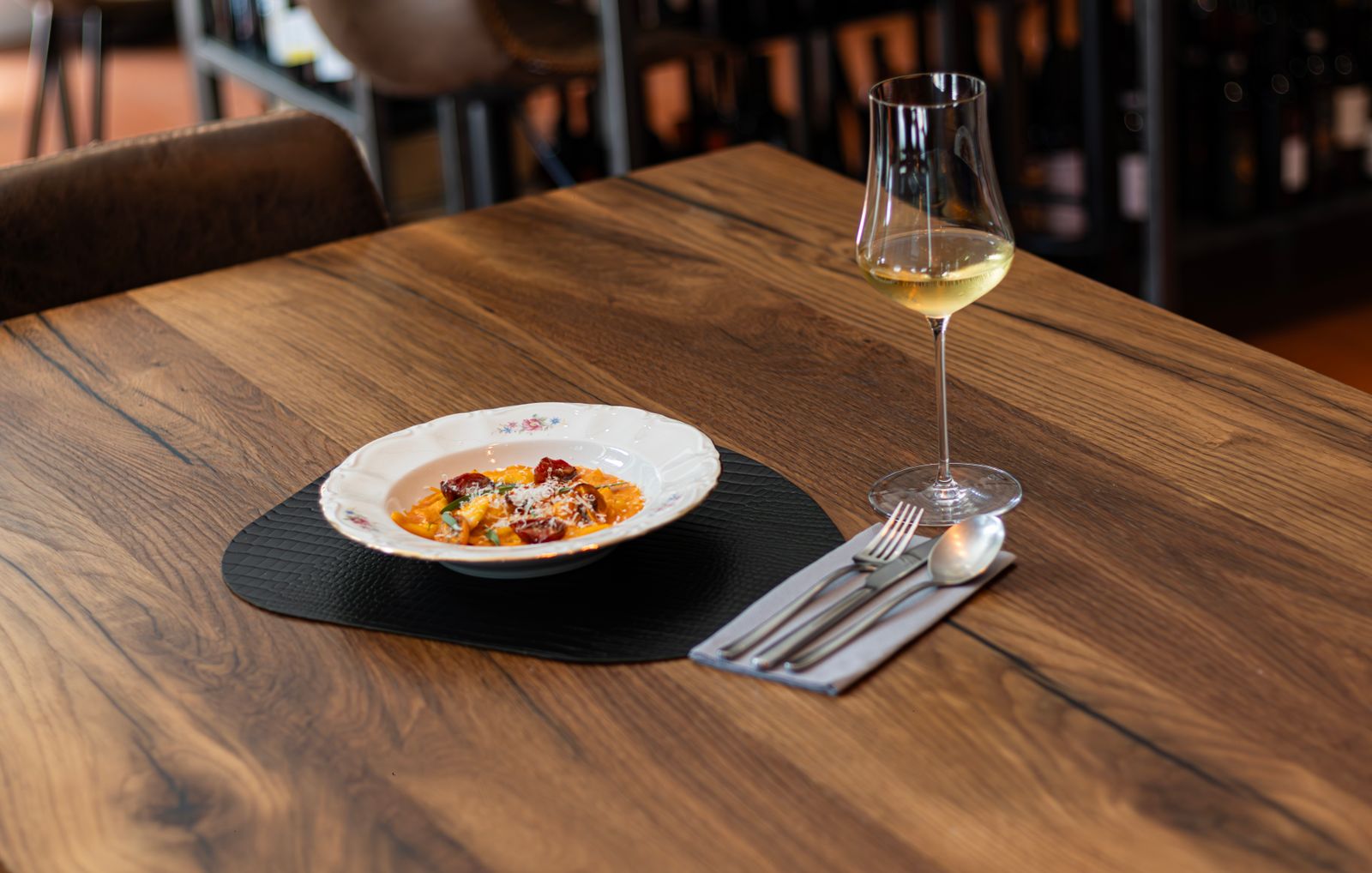 Italian pasta dish and a glass of white wine on a wooden restaurant table