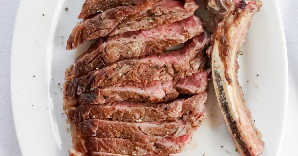 Sliced bone-in ribeye steak on a white platter