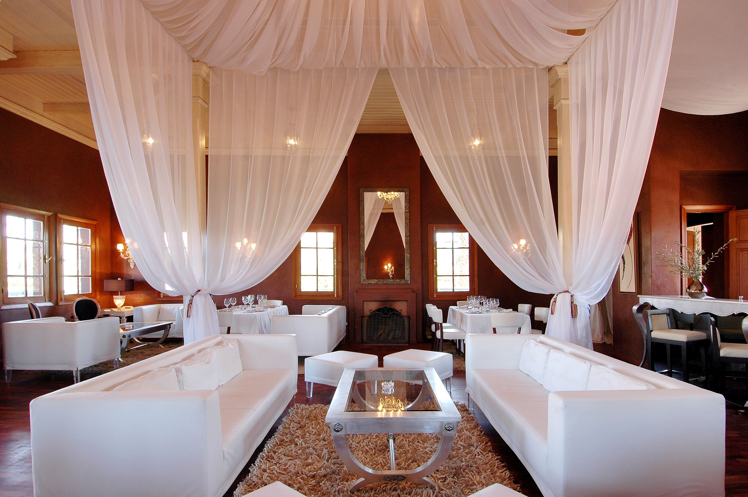 Luxury restaurant dining room with white draped ceilings, white banquettes and tables set for dinner